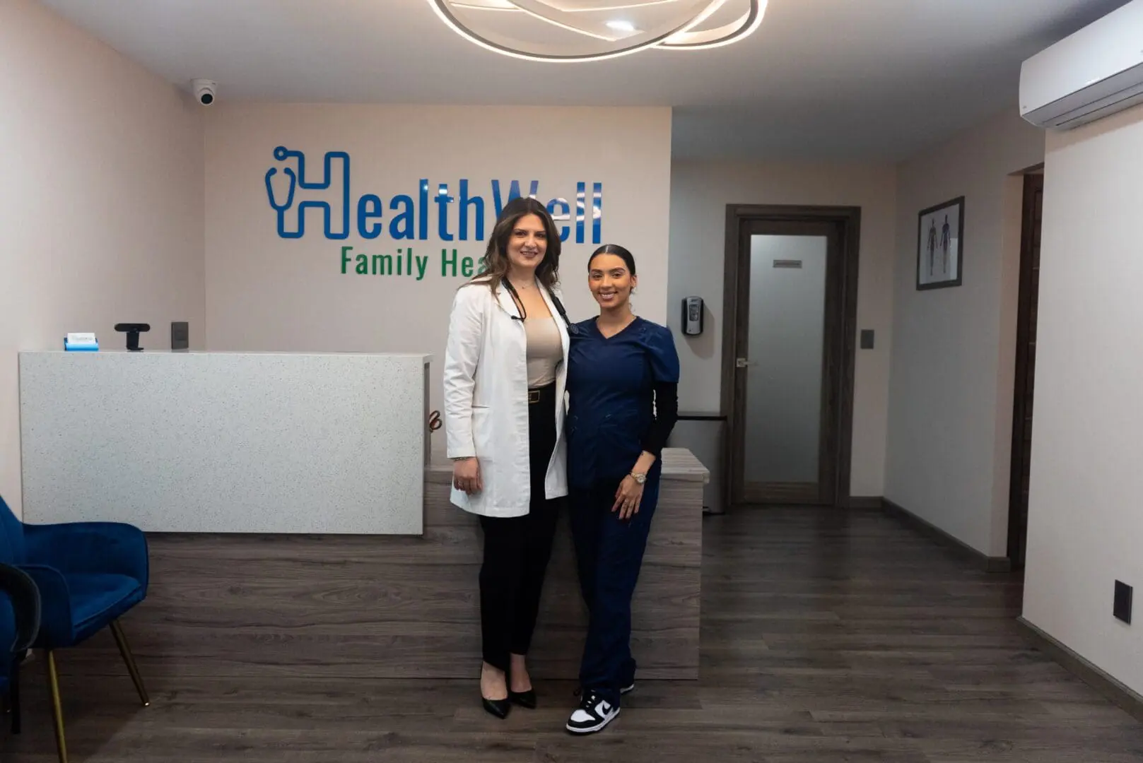 Two women standing in a waiting room of a Primary Care Doctor's office.