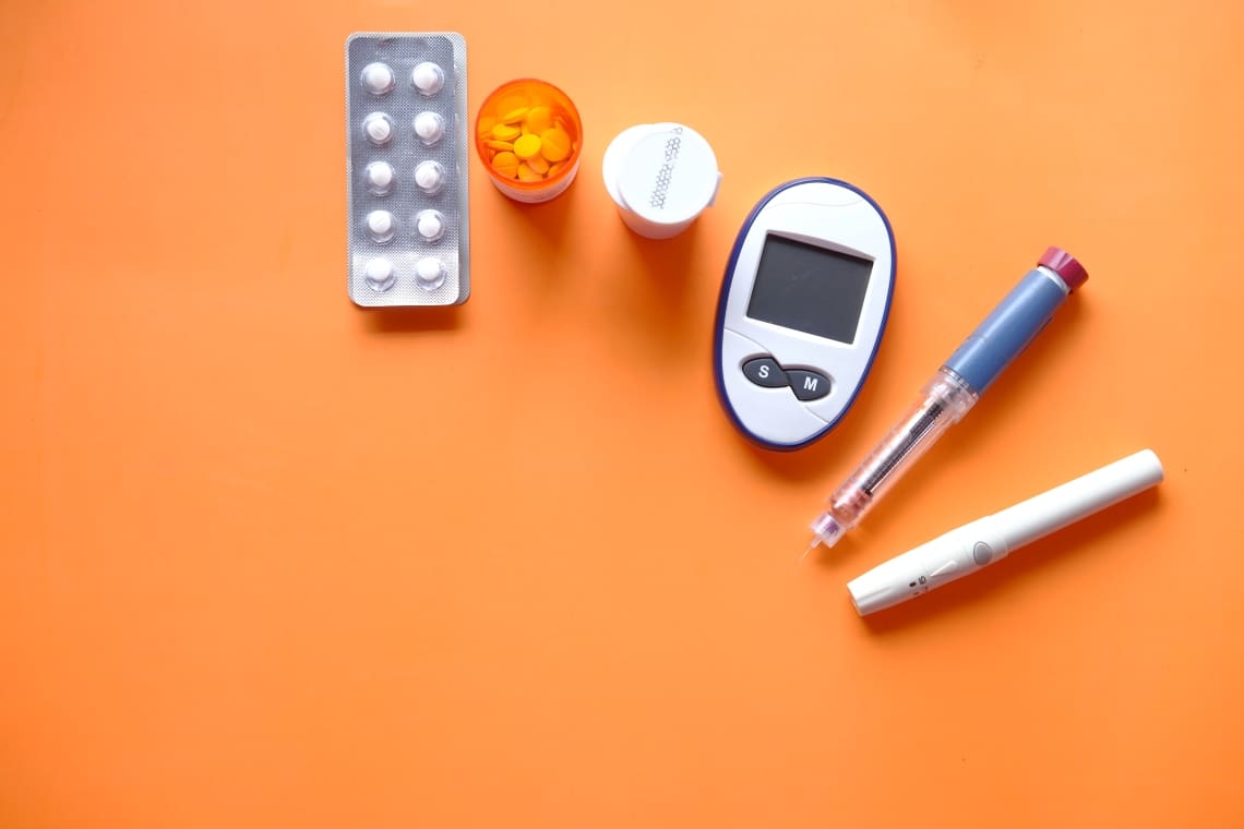 A table with pills, a pill bottle and a glucose meter.
